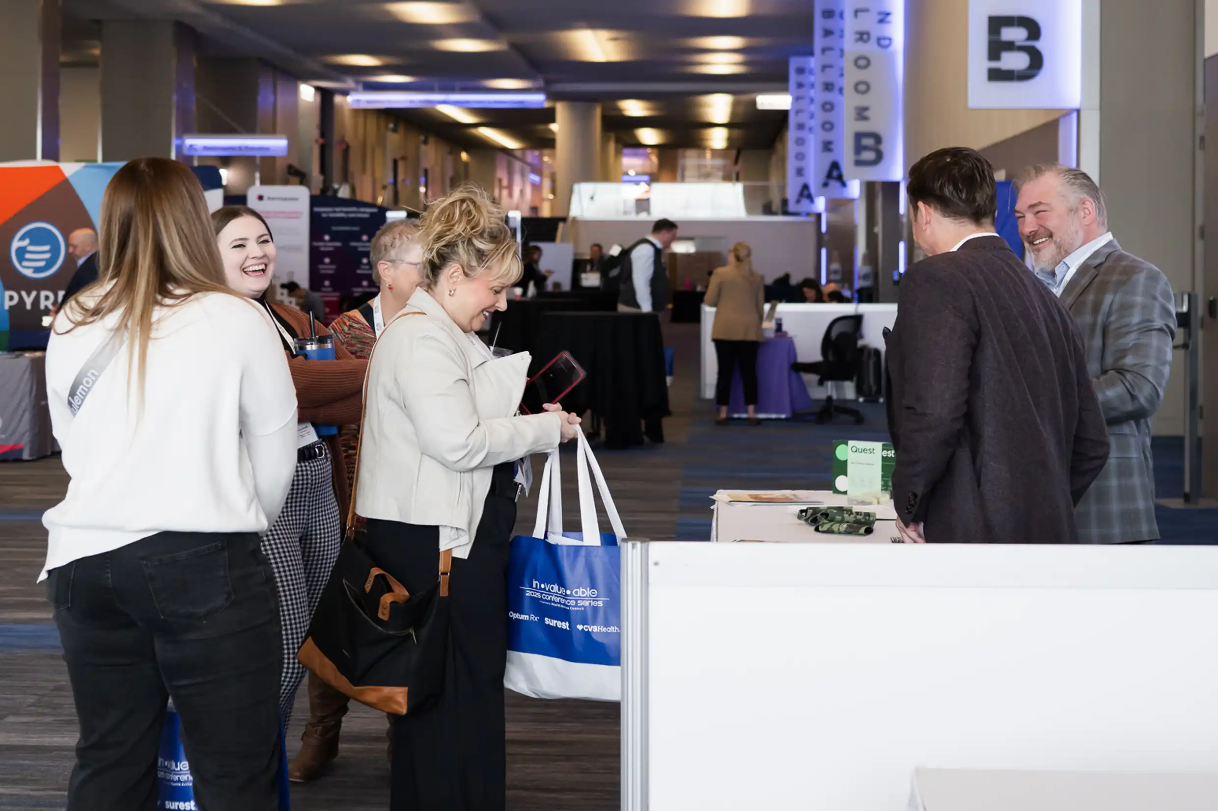 Attendees talking to booths Conference attendees engaging with exhibitors at vendor booths in event expo hall, networking in front of branded displays and Grand Ballroom signage.