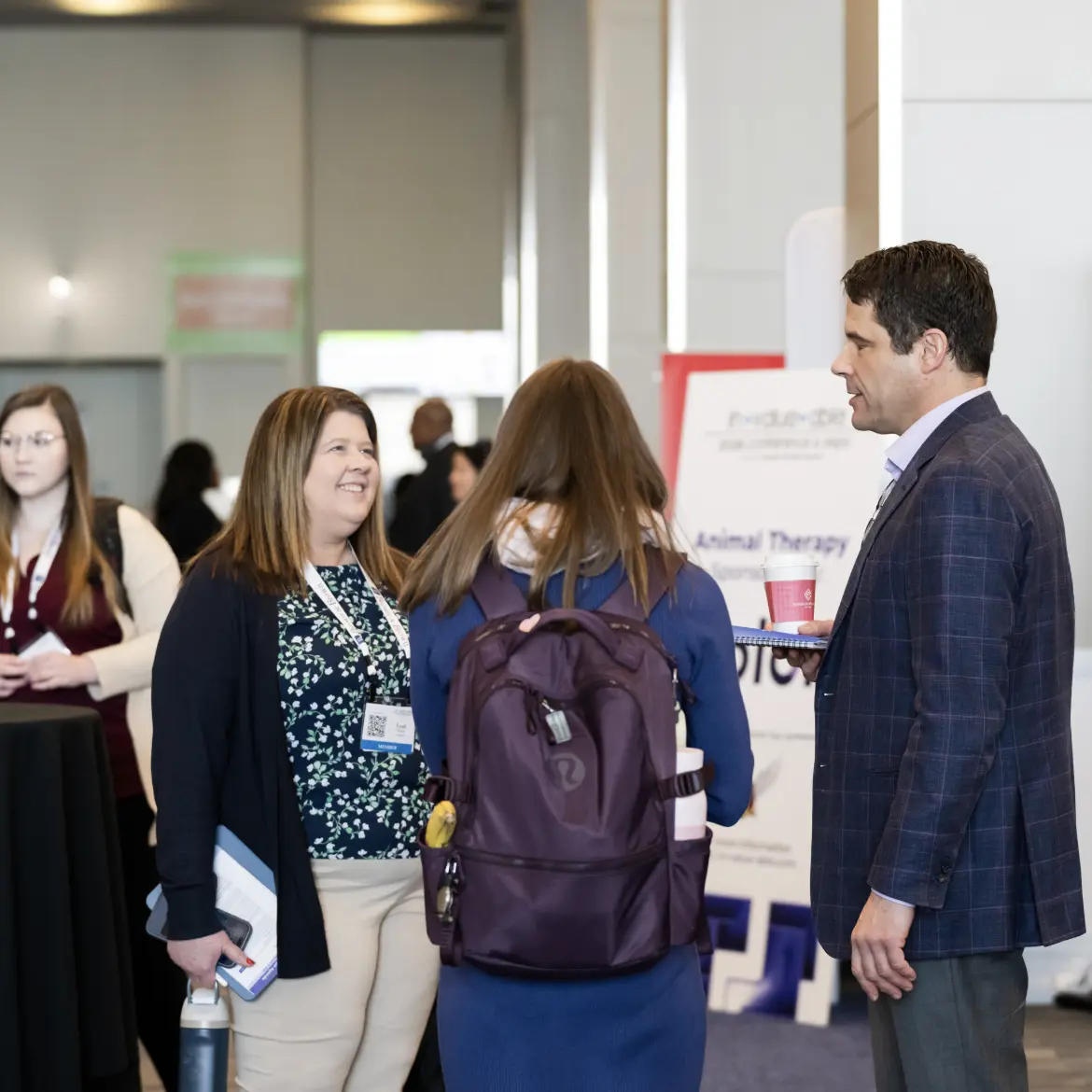 Professional attendees engaging in a networking session at a healthcare industry conference, featuring a woman smiling and a man in a blue blazer holding a coffee cup.
