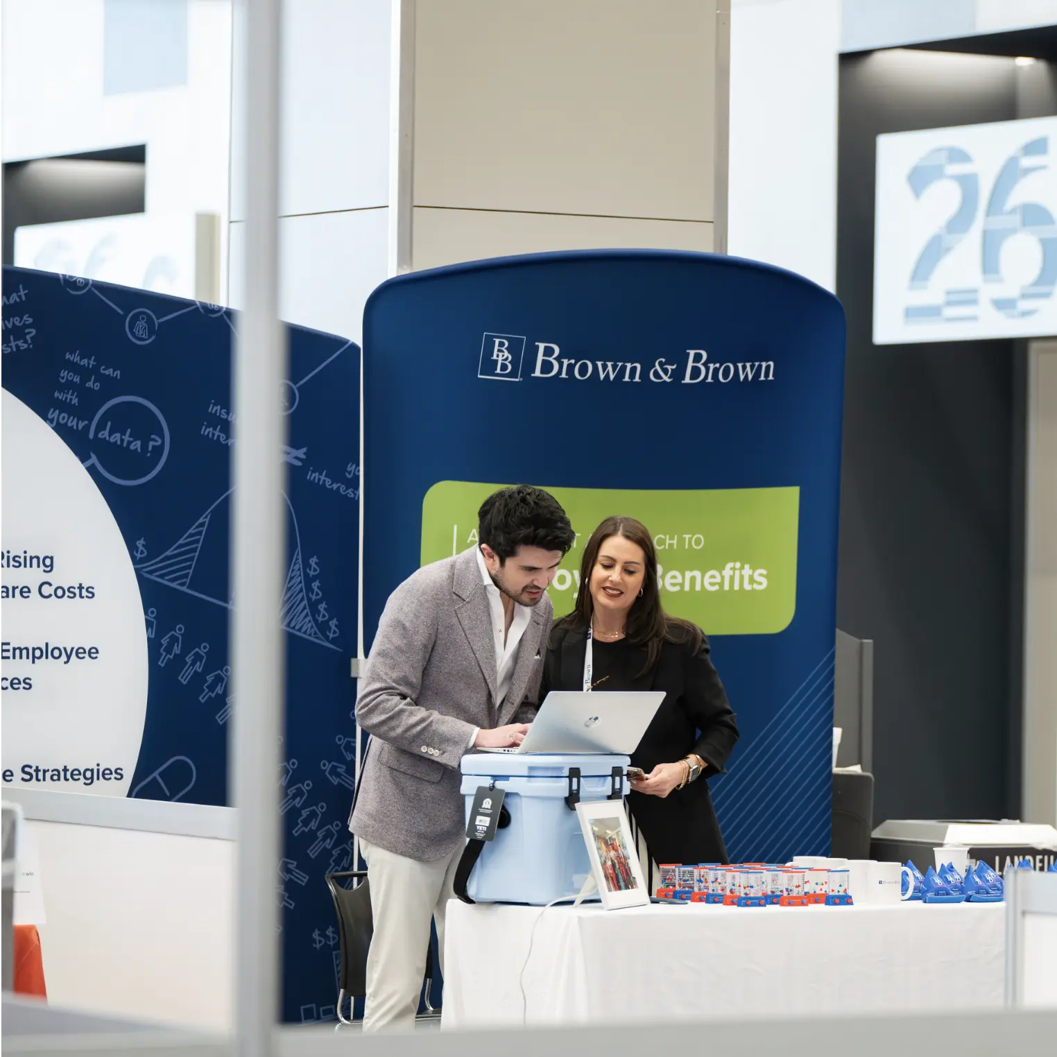 Two business professionals collaborating at a exhibitor booth during a corporate conference, reviewing data on a laptop atop a blue Yeti cooler.